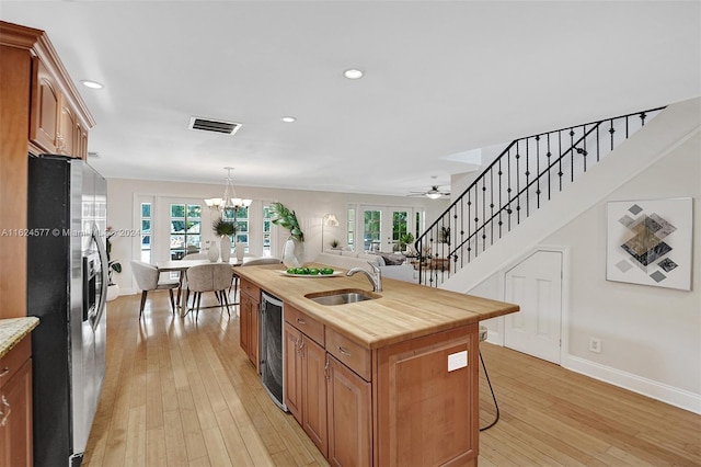 kitchen featuring a sink, a center island with sink, visible vents, stainless steel refrigerator with ice dispenser, and wine cooler