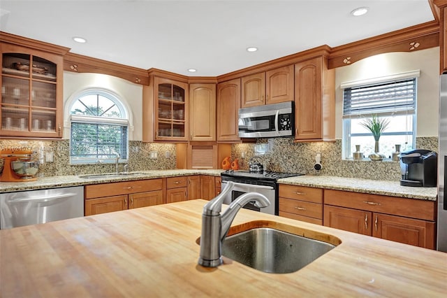 kitchen with stainless steel appliances, a sink, butcher block countertops, and glass insert cabinets