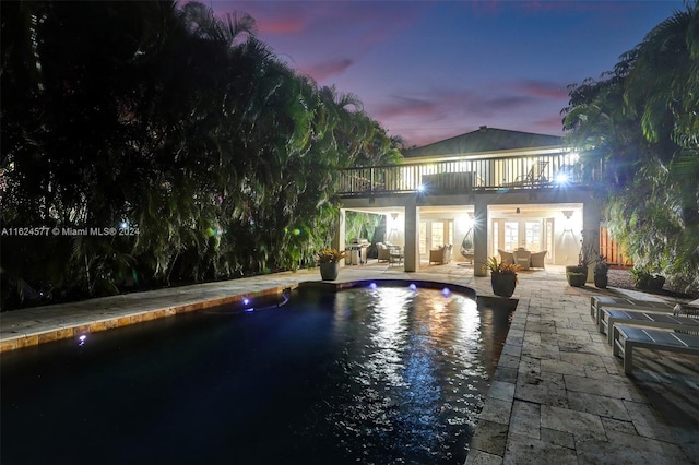 back of house at dusk with a balcony, outdoor lounge area, an outdoor pool, french doors, and a patio