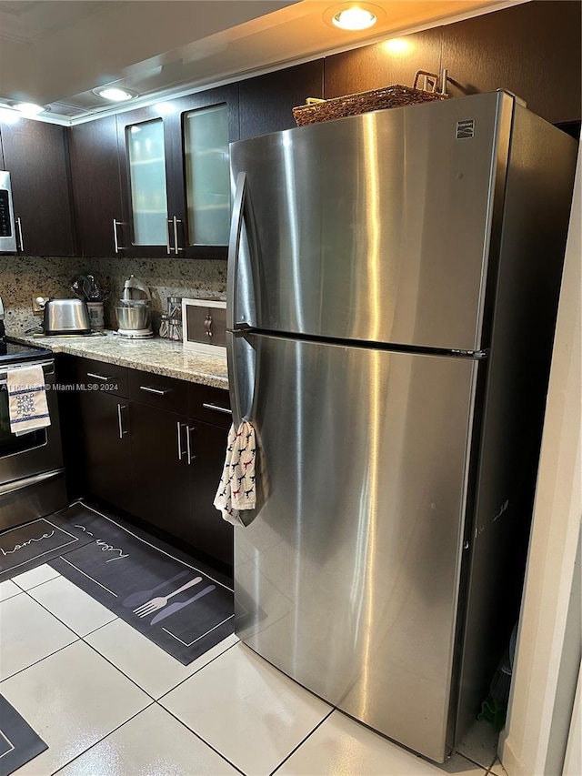 kitchen featuring dark brown cabinetry, appliances with stainless steel finishes, backsplash, and light tile patterned floors