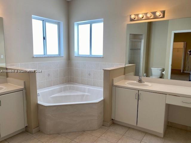 bathroom with vanity, tile patterned flooring, toilet, and a relaxing tiled tub