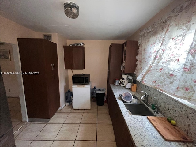 kitchen with light tile patterned flooring, dark brown cabinets, light stone counters, and sink