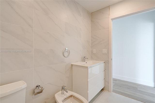 half bathroom featuring a bidet, vanity, toilet, and tile walls