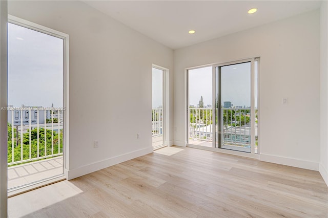 empty room featuring light wood-type flooring, a view of city, baseboards, and recessed lighting