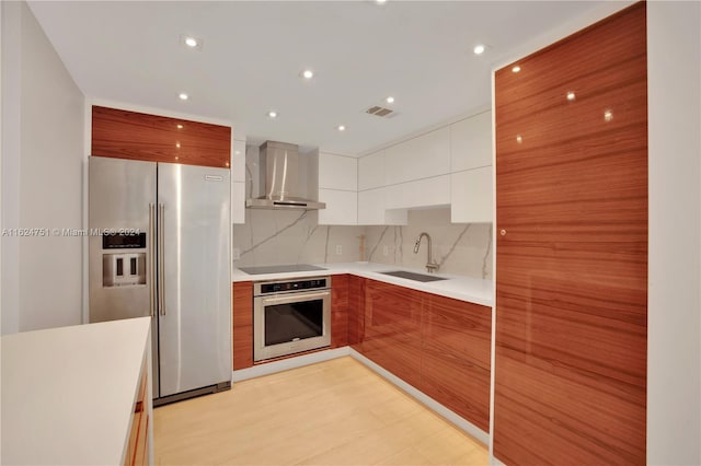 kitchen with appliances with stainless steel finishes, sink, white cabinets, backsplash, and wall chimney exhaust hood