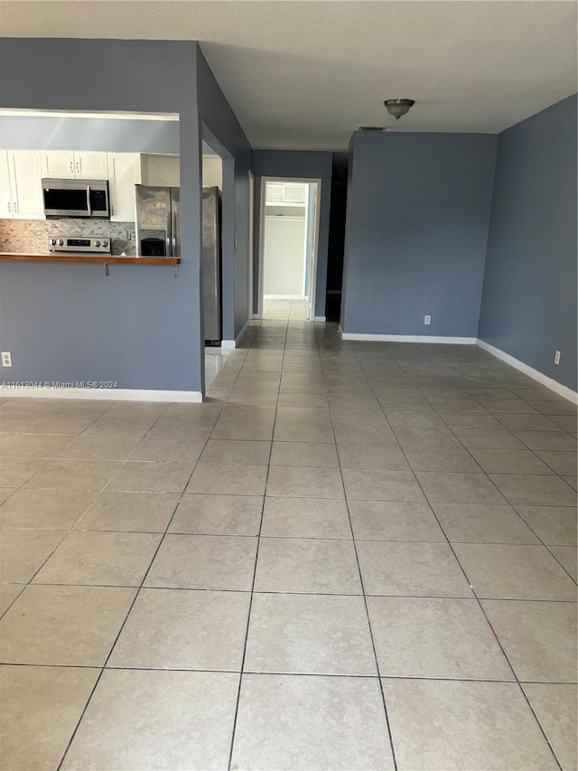 kitchen with white cabinets, stove, light tile patterned floors, and backsplash