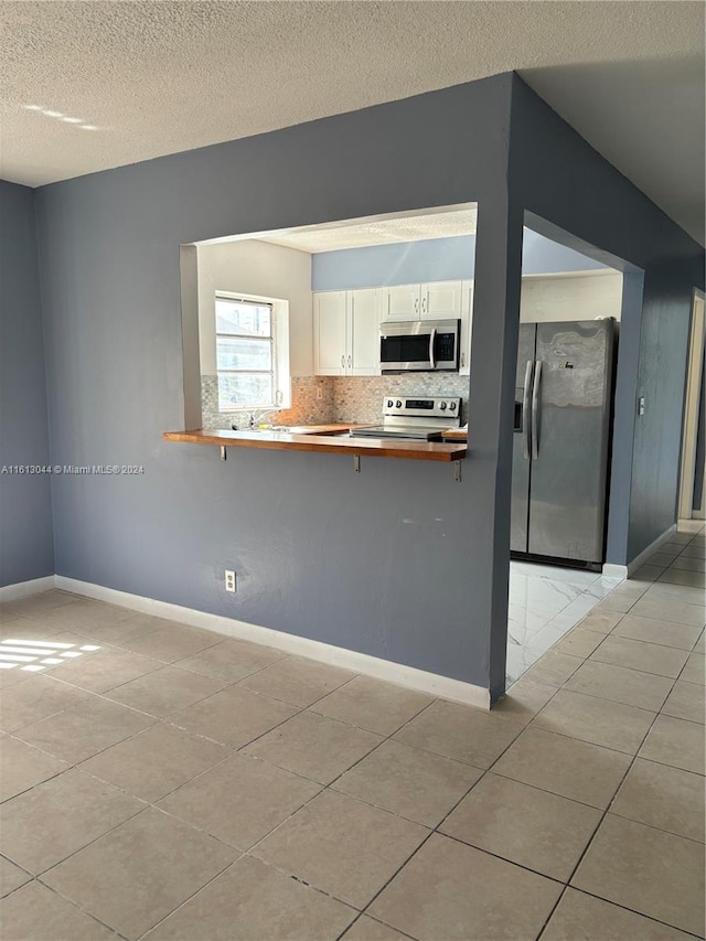 kitchen with white cabinets, appliances with stainless steel finishes, light tile patterned flooring, a kitchen bar, and kitchen peninsula