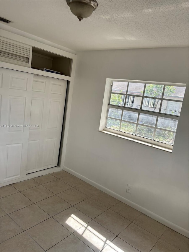 unfurnished bedroom with a closet, light tile patterned floors, and a textured ceiling