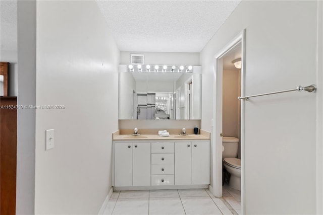 bathroom with toilet, vanity, a textured ceiling, and tile patterned floors