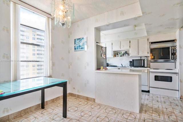 kitchen featuring decorative light fixtures, white cabinets, white appliances, kitchen peninsula, and a chandelier