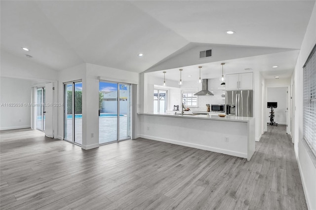 kitchen with wall chimney range hood, appliances with stainless steel finishes, white cabinets, decorative light fixtures, and kitchen peninsula