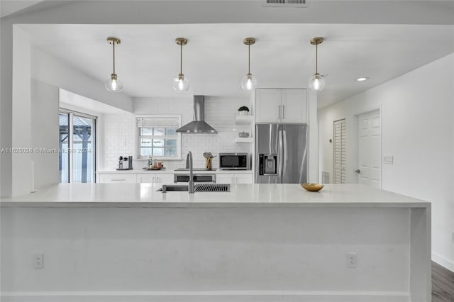 kitchen with white cabinets, backsplash, hanging light fixtures, stainless steel appliances, and wall chimney range hood