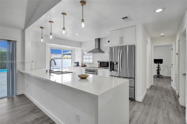 kitchen featuring white cabinetry, kitchen peninsula, pendant lighting, stainless steel appliances, and wall chimney range hood