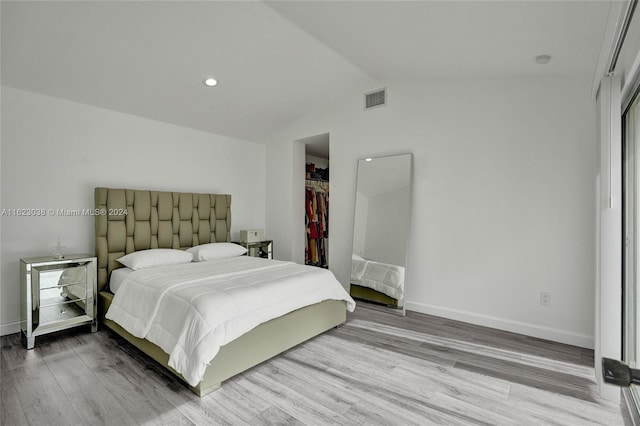 bedroom with vaulted ceiling, a walk in closet, light hardwood / wood-style flooring, and a closet