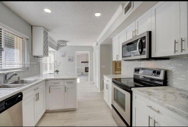 kitchen featuring stainless steel appliances, white cabinets, decorative backsplash, light wood-type flooring, and a textured ceiling