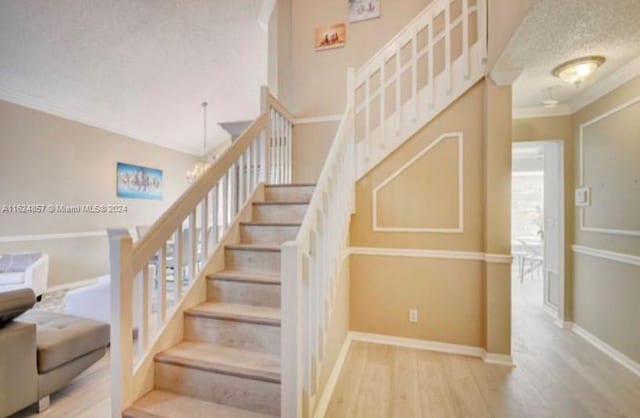 stairway with a textured ceiling, crown molding, light wood-type flooring, and a chandelier