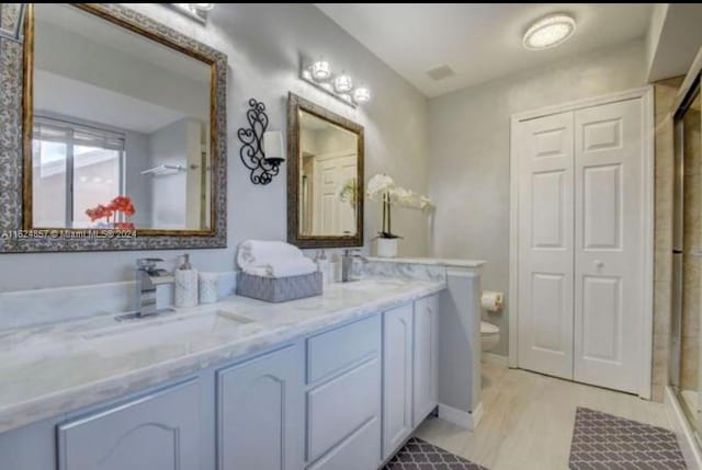 bathroom with dual vanity, a shower with door, and toilet