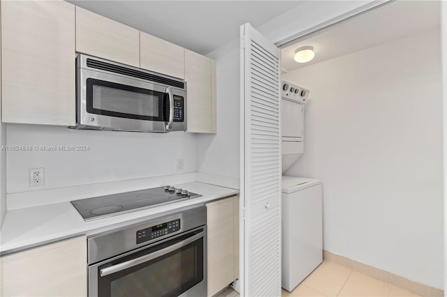 kitchen with light tile patterned flooring, stainless steel appliances, stacked washer / drying machine, and cream cabinets