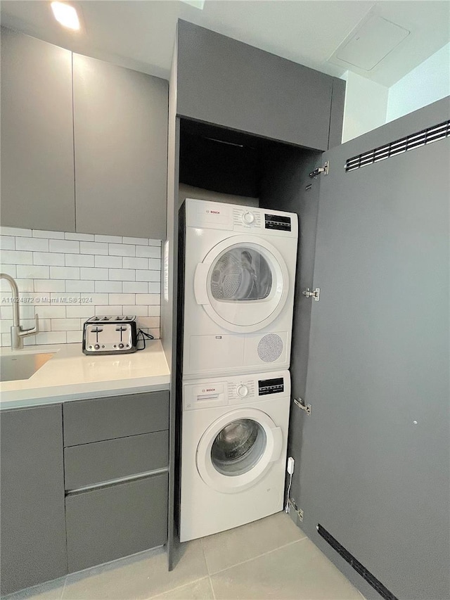 laundry area featuring sink, light tile patterned floors, and stacked washer / dryer