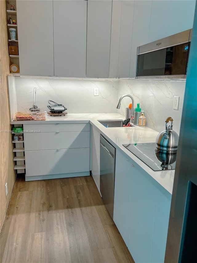 kitchen with light hardwood / wood-style flooring, tasteful backsplash, sink, dishwasher, and black electric stovetop