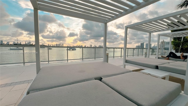 patio terrace at dusk featuring a pergola and a water view