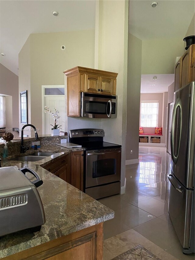 kitchen with dark stone countertops, high vaulted ceiling, kitchen peninsula, sink, and appliances with stainless steel finishes