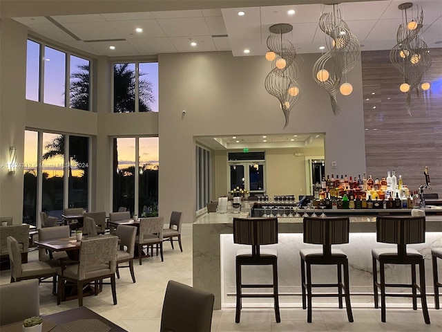 interior space with a breakfast bar area, a notable chandelier, hanging light fixtures, a towering ceiling, and light tile patterned flooring