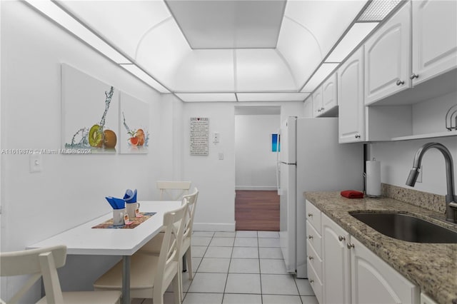 kitchen featuring white refrigerator, sink, light stone counters, light tile patterned flooring, and white cabinetry