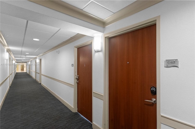 corridor featuring dark carpet, ornamental molding, and a drop ceiling