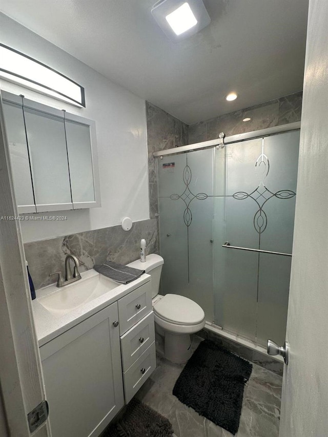 bathroom featuring a shower with door, vanity, tile walls, and toilet