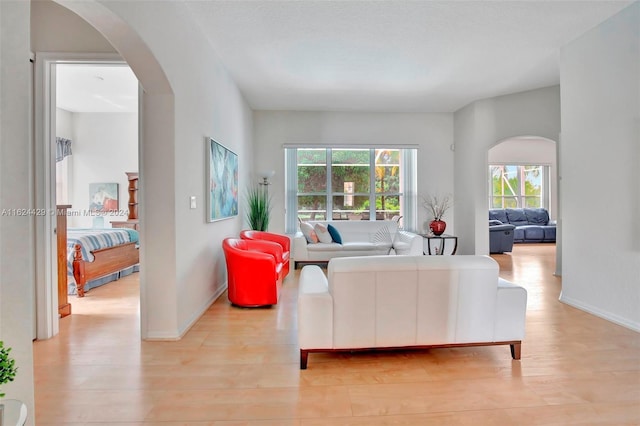 living room featuring baseboards, arched walkways, and light wood-style flooring