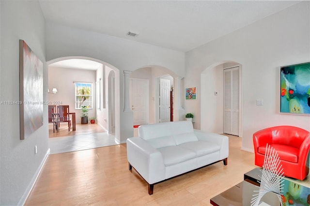 living room with baseboards, visible vents, arched walkways, and light wood-type flooring