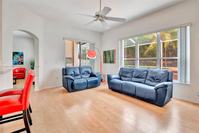 living room with light wood-style flooring, baseboards, arched walkways, and ceiling fan