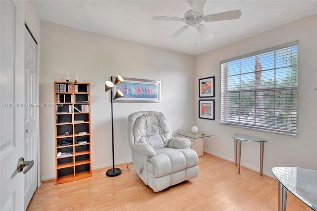 living area with a ceiling fan, wood finished floors, and baseboards