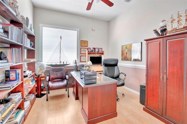 office area with a ceiling fan, light wood-style flooring, and wainscoting