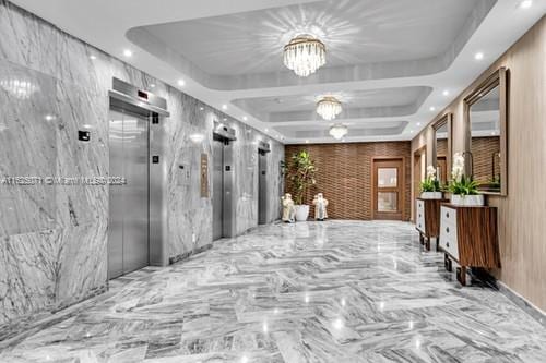 hallway featuring a chandelier, elevator, and a raised ceiling