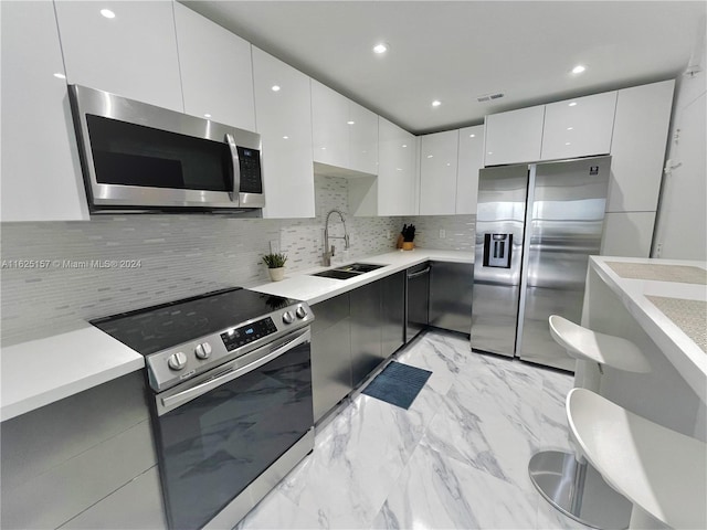 kitchen with stainless steel appliances, white cabinets, sink, backsplash, and light tile patterned floors