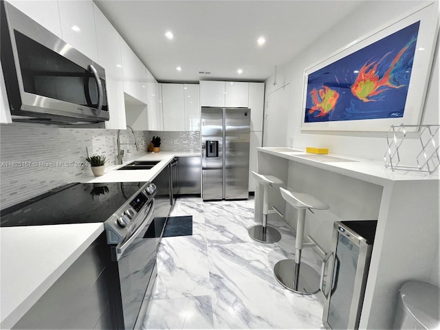 kitchen featuring white cabinetry, sink, appliances with stainless steel finishes, light tile patterned floors, and backsplash