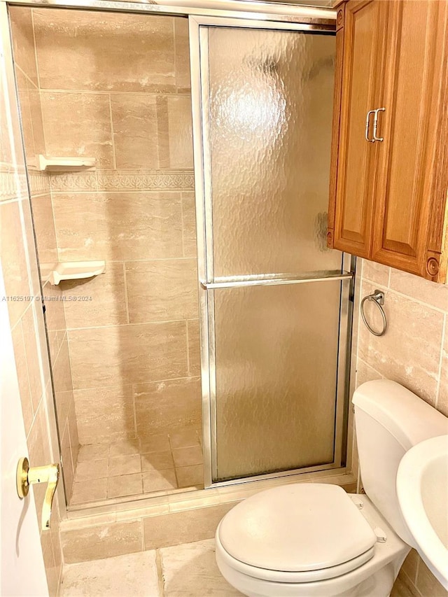 bathroom featuring an enclosed shower, toilet, and tile walls