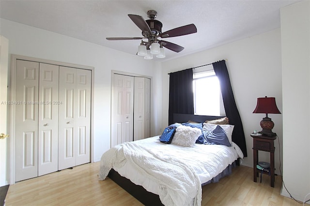 bedroom featuring ceiling fan, light hardwood / wood-style flooring, and multiple closets