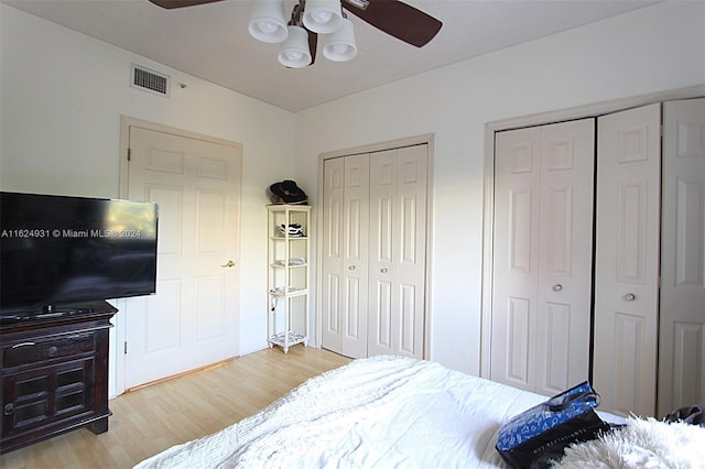 bedroom with ceiling fan, light hardwood / wood-style floors, and multiple closets