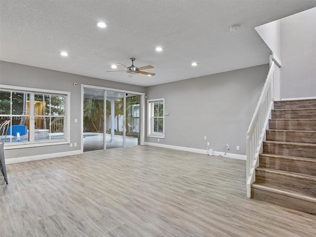 unfurnished living room featuring ceiling fan, a textured ceiling, a healthy amount of sunlight, and light hardwood / wood-style flooring