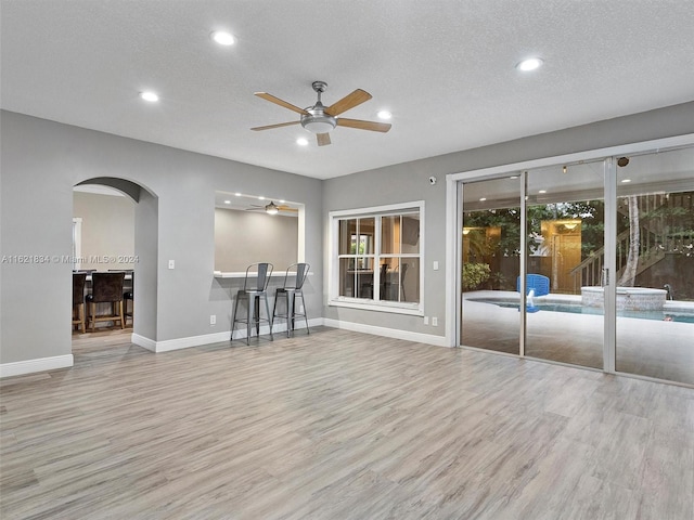 unfurnished living room with light hardwood / wood-style floors, ceiling fan, and a textured ceiling