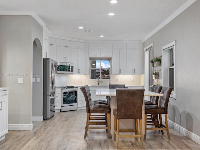 kitchen with white cabinets, a kitchen breakfast bar, appliances with stainless steel finishes, and light hardwood / wood-style floors