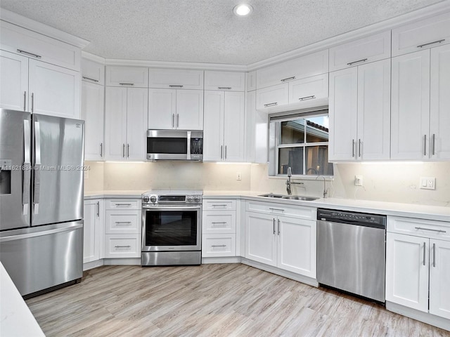 kitchen with stainless steel appliances, sink, a textured ceiling, white cabinets, and light wood-type flooring