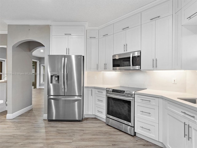 kitchen featuring appliances with stainless steel finishes, a textured ceiling, light hardwood / wood-style floors, and white cabinets