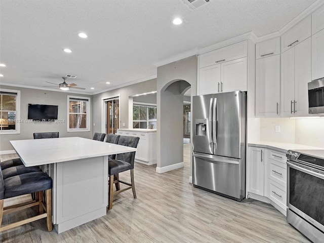 kitchen with white cabinetry, appliances with stainless steel finishes, ceiling fan, a breakfast bar area, and a textured ceiling