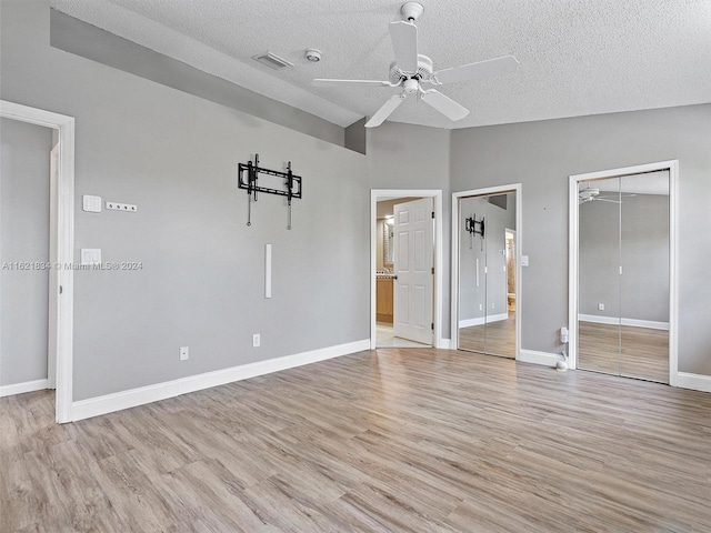 unfurnished bedroom featuring a textured ceiling, light wood-type flooring, ceiling fan, and two closets