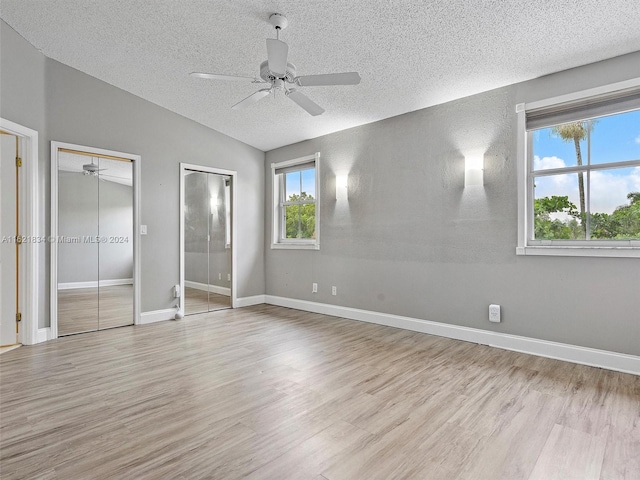 unfurnished bedroom featuring a textured ceiling, vaulted ceiling, light hardwood / wood-style floors, multiple closets, and ceiling fan