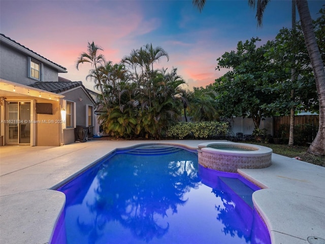 pool at dusk with a patio area and an in ground hot tub